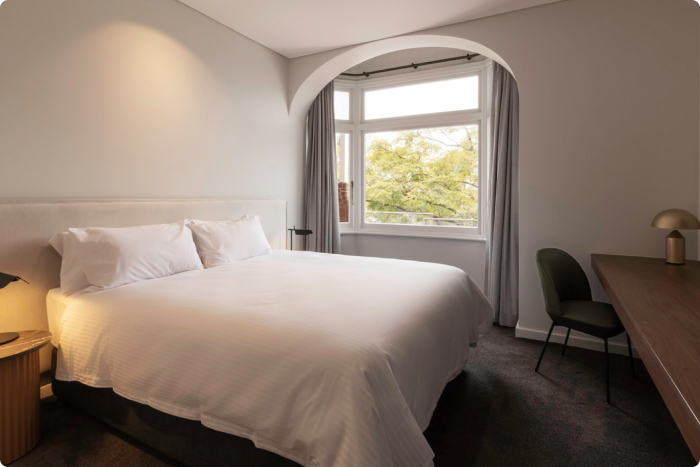 Harbour View Room - bedroom with a window view of the harbour, double bed and desk lamp, on the right is a work desk, TV and chair.