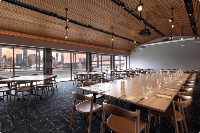 Dining Room - with tables and chairs and a large balcony overlooking a view of the Sydney Harbour Bridge at dusk.